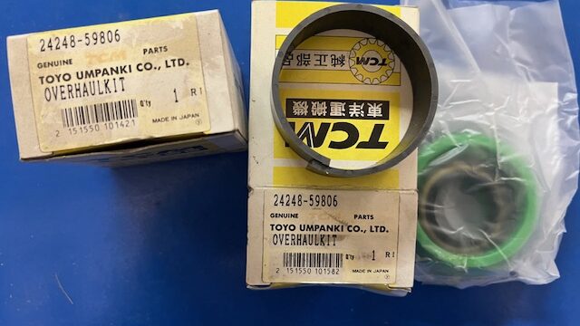 Two beige tool-part boxes labeled 24248-59806 Genuine Parts Toyo Umpanki Co., Ltd. Overhaul Kit, with a black circular ring resting on the lid of one box and a clear plastic bag containing a green seal ring nearby.