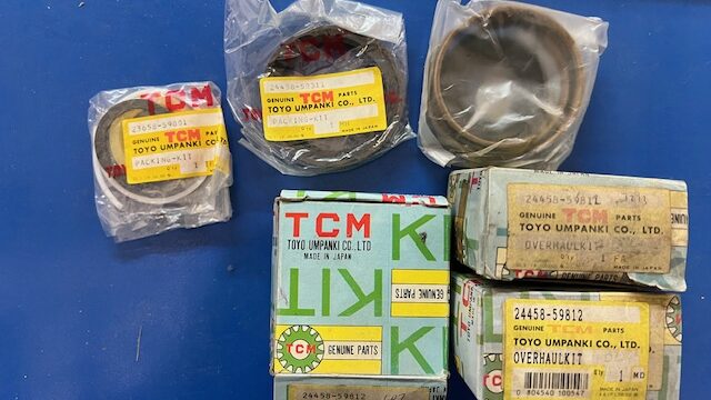 Assortment of TCM genuine parts boxes and two wrapped circular bearings on a blue surface.