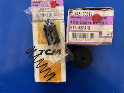 TCM repair kit parts on a blue surface, with a small black plastic component in a bag and a purple-labeled box nearby.
