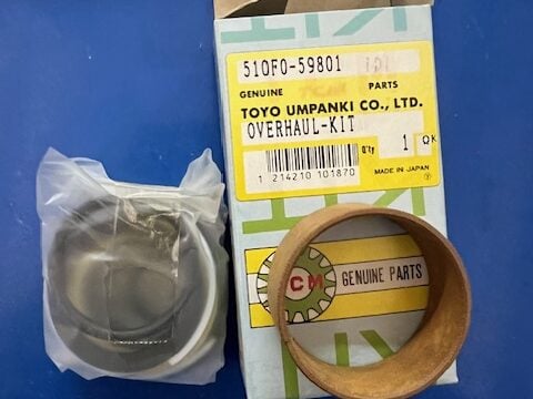 Overhaul kit box labeled Toyo Umpanki Co. parts, with piston ring and brown bearing placed beside it on a blue surface