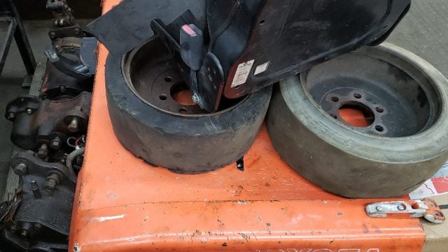 Two worn black tires sit on an orange metal work surface in a workshop, with machinery visible in the background.
